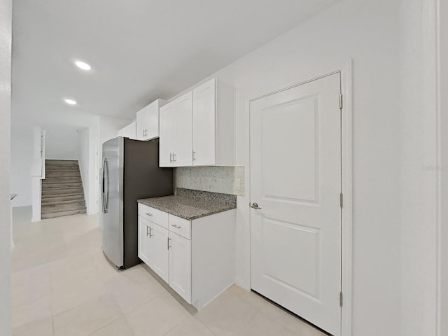 kitchen featuring white cabinetry, light tile patterned floors, decorative backsplash, dark stone counters, and stainless steel fridge