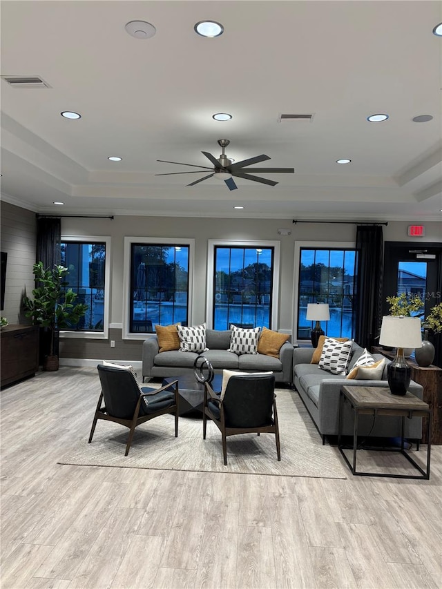 living room featuring ceiling fan, light hardwood / wood-style flooring, ornamental molding, and a raised ceiling