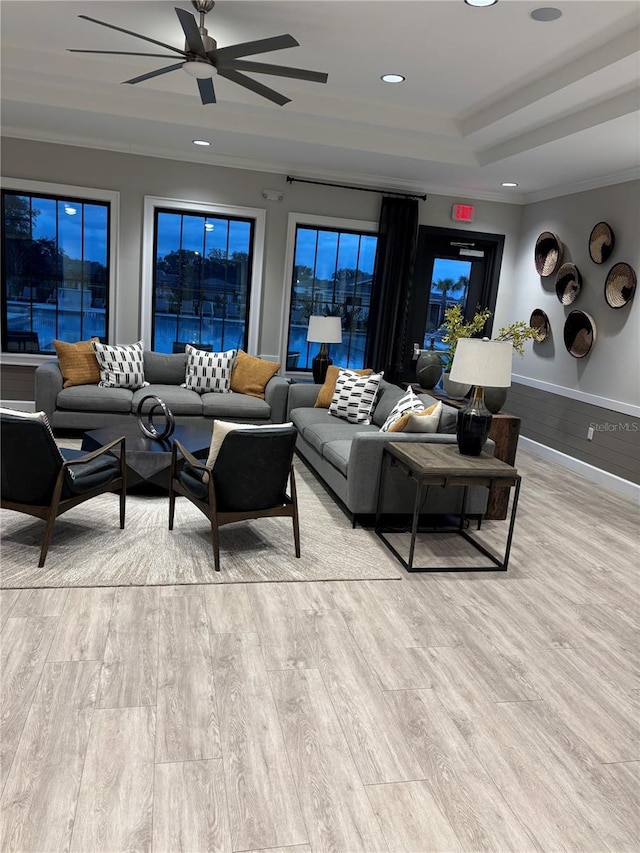 living room featuring ceiling fan, ornamental molding, light hardwood / wood-style flooring, and a tray ceiling