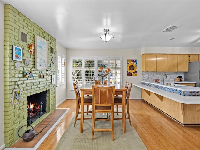 dining room featuring sink, light hardwood / wood-style flooring, and a brick fireplace