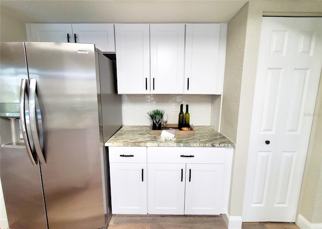 kitchen featuring decorative backsplash, stainless steel fridge with ice dispenser, light wood-style flooring, light stone counters, and white cabinetry