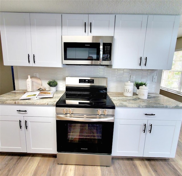 kitchen featuring light stone counters, backsplash, appliances with stainless steel finishes, light wood-style floors, and white cabinetry