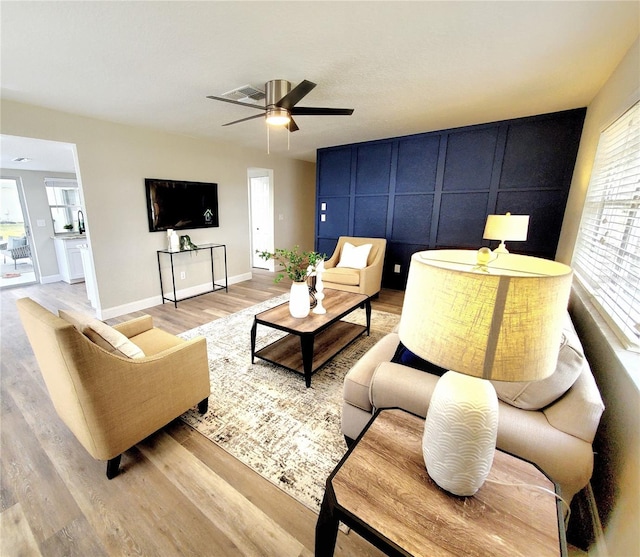 living area with light wood finished floors, visible vents, baseboards, and a ceiling fan