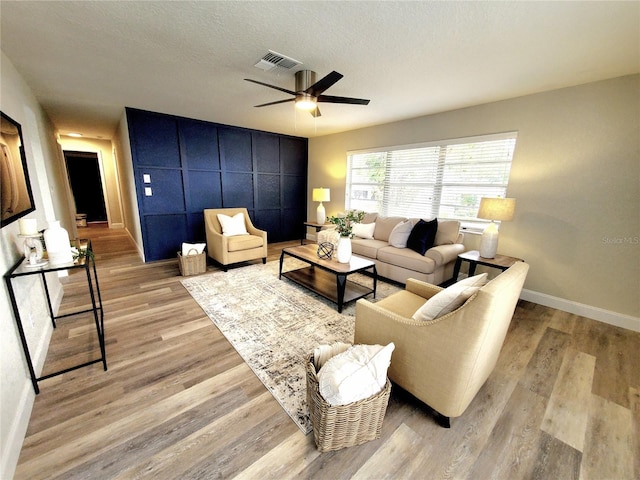 living room featuring a textured ceiling, light wood-type flooring, visible vents, and baseboards