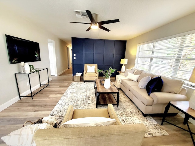 living room with ceiling fan, light wood-style flooring, visible vents, and baseboards