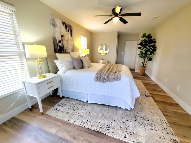 bedroom featuring a ceiling fan, visible vents, baseboards, and wood finished floors