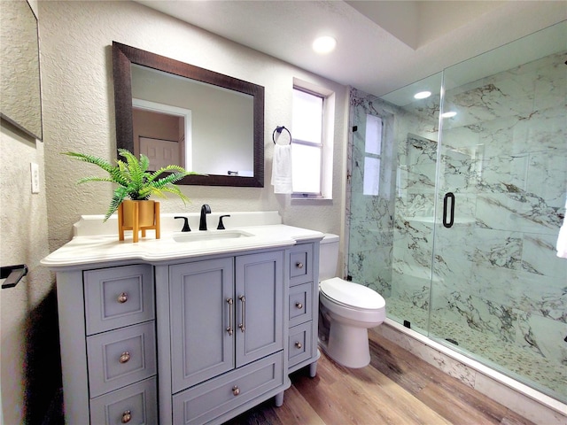 full bathroom with a textured wall, toilet, wood finished floors, vanity, and a marble finish shower