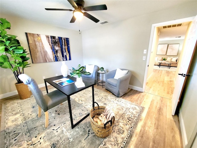 office space featuring a ceiling fan, baseboards, visible vents, and light wood finished floors