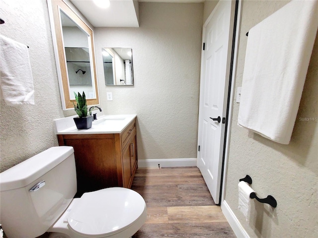 bathroom featuring toilet, a textured wall, wood finished floors, and vanity