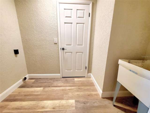 laundry area with a textured wall, laundry area, light wood finished floors, and baseboards