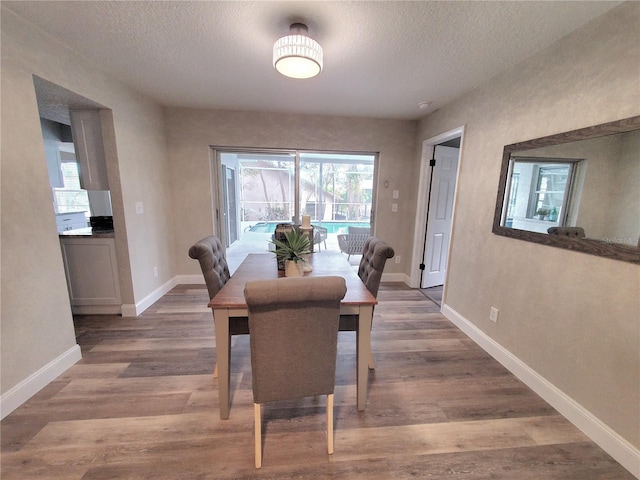 dining space with a textured ceiling, baseboards, and wood finished floors