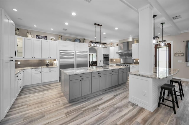 kitchen featuring white cabinets, wall chimney exhaust hood, decorative light fixtures, and a large island with sink