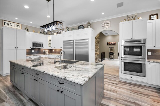 kitchen with gray cabinetry, stainless steel appliances, sink, a center island with sink, and hanging light fixtures