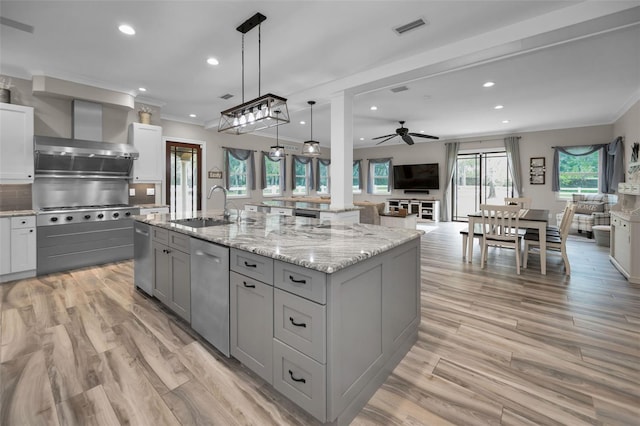 kitchen featuring sink, hanging light fixtures, wall chimney exhaust hood, ceiling fan, and an island with sink