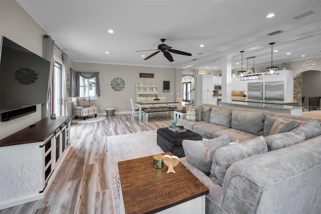 living room featuring light wood-type flooring, ceiling fan, and crown molding