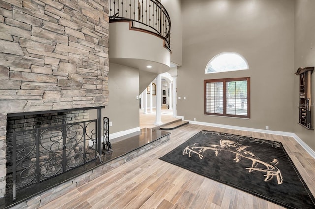 entrance foyer featuring hardwood / wood-style floors, a stone fireplace, and a towering ceiling