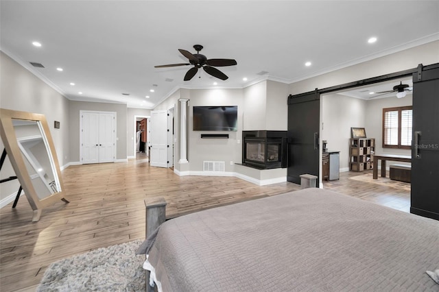 bedroom with ceiling fan, a barn door, light hardwood / wood-style flooring, a closet, and ornamental molding