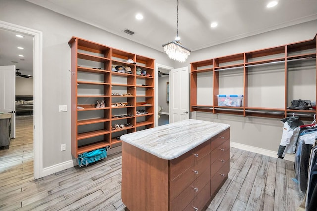 spacious closet featuring ceiling fan with notable chandelier and light wood-type flooring