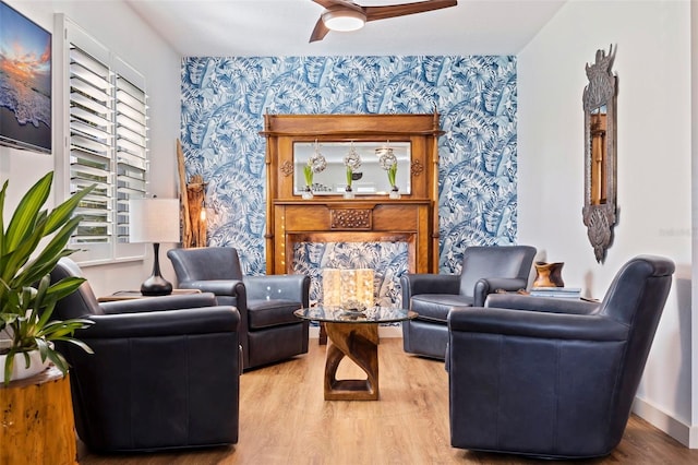 living area with a ceiling fan, wood finished floors, baseboards, and wallpapered walls