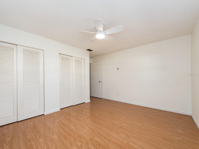 unfurnished bedroom featuring multiple closets, ceiling fan, and light hardwood / wood-style flooring