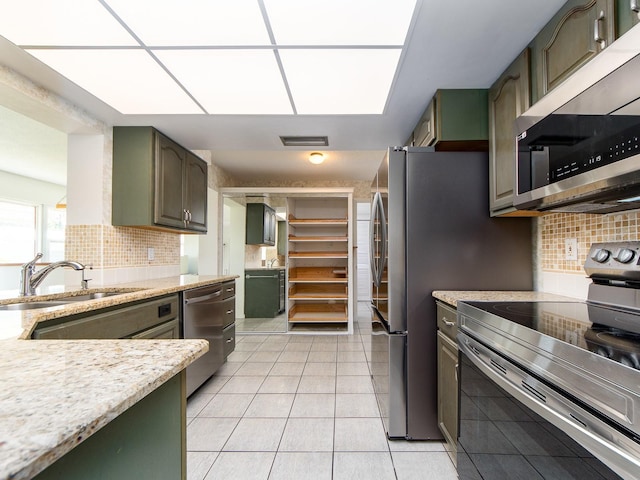 kitchen with sink, light tile patterned floors, green cabinets, appliances with stainless steel finishes, and tasteful backsplash