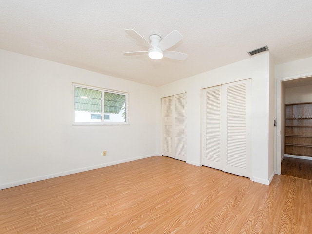 unfurnished bedroom with two closets, ceiling fan, and light hardwood / wood-style floors