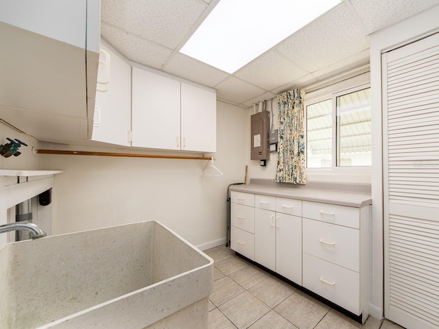 kitchen featuring sink, light tile patterned floors, a paneled ceiling, white cabinetry, and electric panel