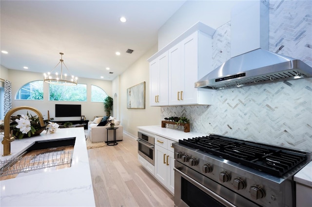 kitchen featuring wall chimney range hood, light hardwood / wood-style flooring, decorative backsplash, white cabinets, and appliances with stainless steel finishes