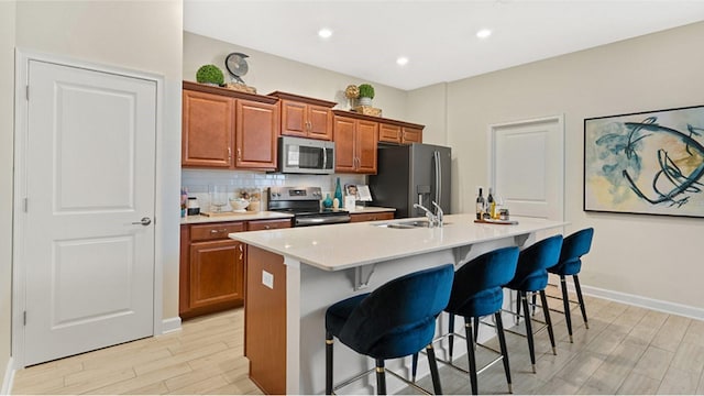 kitchen featuring a center island with sink, sink, appliances with stainless steel finishes, tasteful backsplash, and a kitchen bar