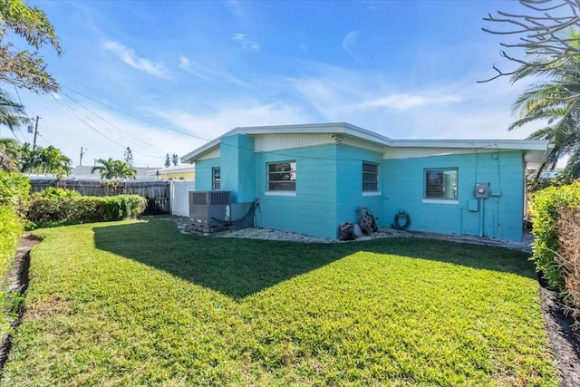 back of property with central AC unit, fence, and a lawn