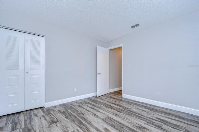 unfurnished bedroom with light wood-type flooring, a closet, and a textured ceiling