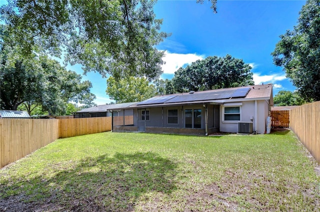 rear view of property featuring a lawn, central AC, solar panels, and a sunroom