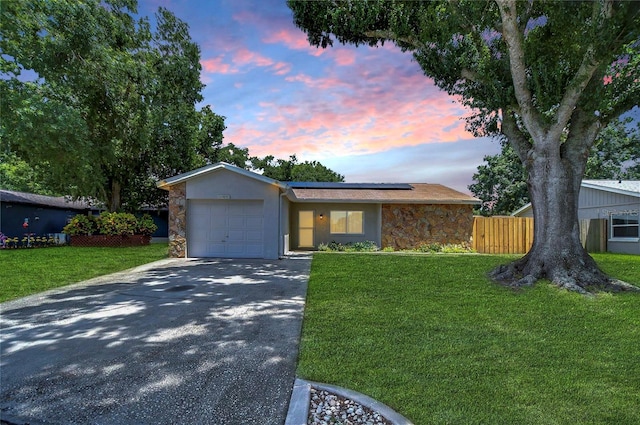 single story home with a garage, a lawn, and solar panels