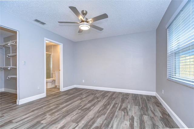 unfurnished bedroom with ceiling fan, hardwood / wood-style flooring, a spacious closet, a textured ceiling, and a closet