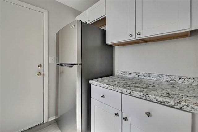 kitchen featuring light stone counters, white cabinetry, light wood-type flooring, and stainless steel refrigerator