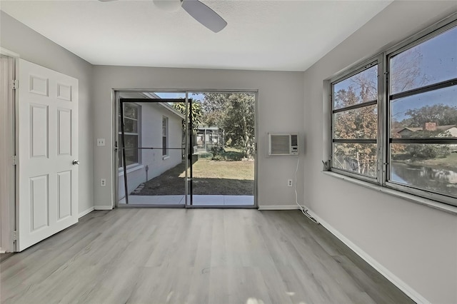 spare room with light hardwood / wood-style floors, a wall unit AC, and ceiling fan