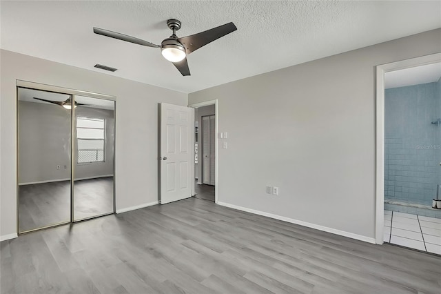 unfurnished bedroom with a textured ceiling, ceiling fan, connected bathroom, light hardwood / wood-style floors, and a closet