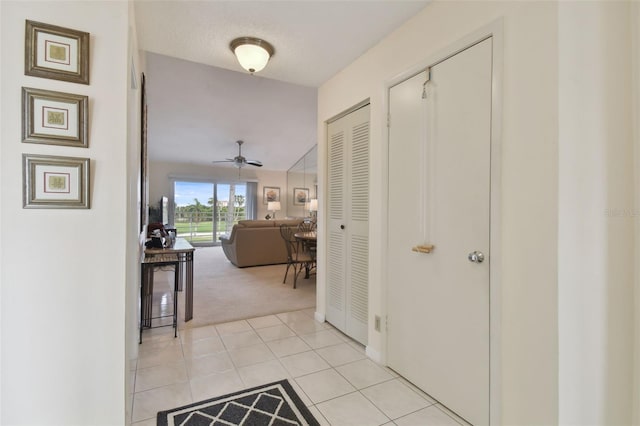 hallway with a textured ceiling, light colored carpet, and vaulted ceiling