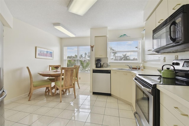 kitchen featuring sink, stainless steel electric range oven, cream cabinetry, dishwashing machine, and light tile patterned flooring