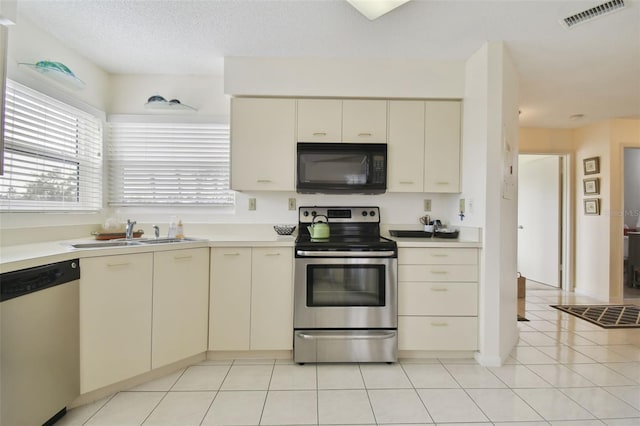 kitchen featuring sink, a textured ceiling, cream cabinetry, light tile patterned flooring, and appliances with stainless steel finishes