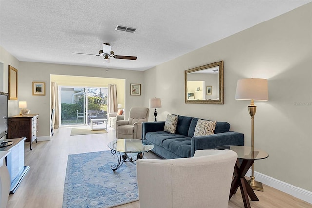 living room with ceiling fan, light wood-type flooring, and a textured ceiling