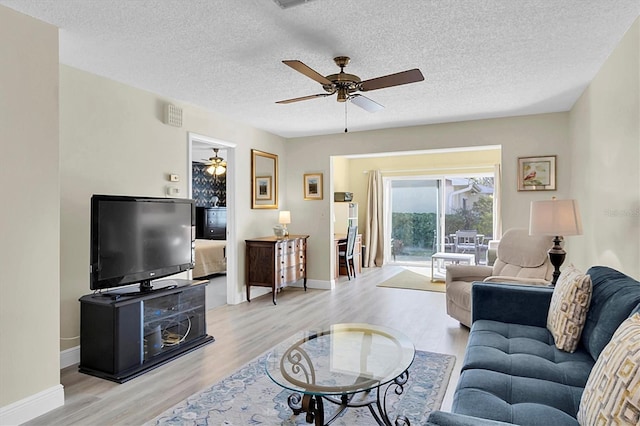 living room with ceiling fan, a textured ceiling, and light wood-type flooring