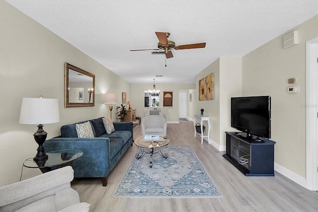 living room with ceiling fan with notable chandelier, a textured ceiling, and light hardwood / wood-style flooring