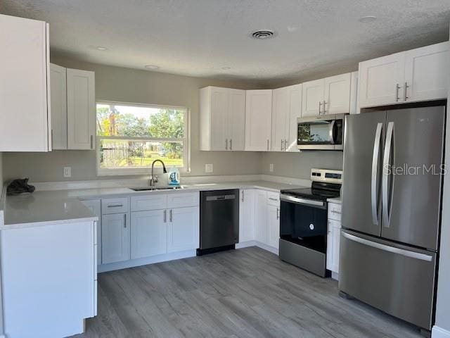 kitchen with white cabinets, appliances with stainless steel finishes, light wood-type flooring, and sink