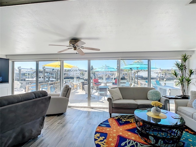 living room featuring a water view, ceiling fan, light hardwood / wood-style floors, and a textured ceiling