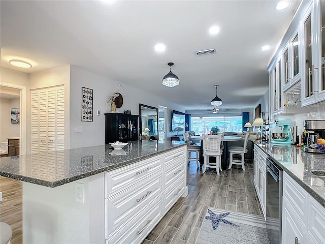 kitchen with ceiling fan, dark stone countertops, hanging light fixtures, a center island, and white cabinets