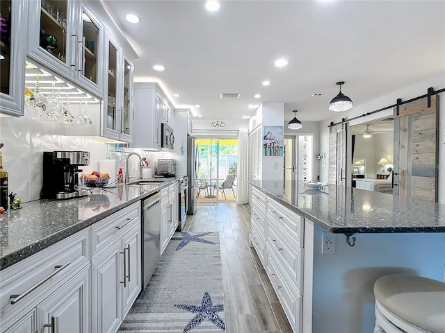 kitchen featuring a kitchen island, a breakfast bar, white cabinetry, stainless steel appliances, and a barn door