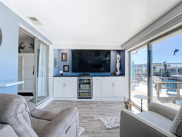 living room with bar, beverage cooler, and light wood-type flooring