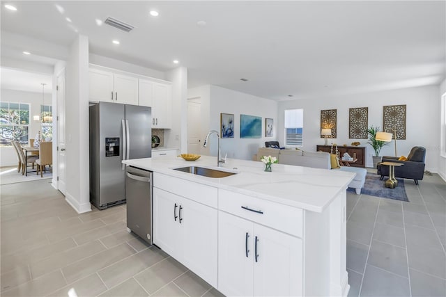 kitchen with white cabinets, a center island with sink, sink, light stone countertops, and stainless steel appliances