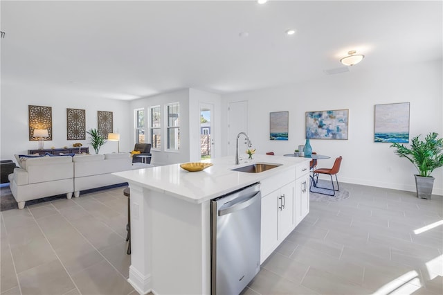 kitchen with stainless steel dishwasher, sink, light tile patterned floors, a center island with sink, and white cabinets